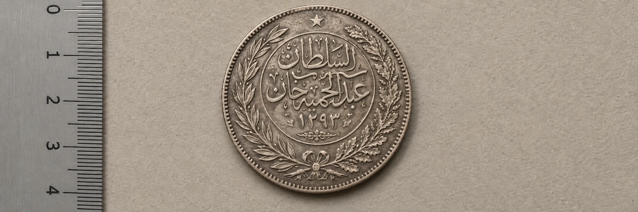 Arabic coin photographed flat with calligraphy, numerals, and a ruler